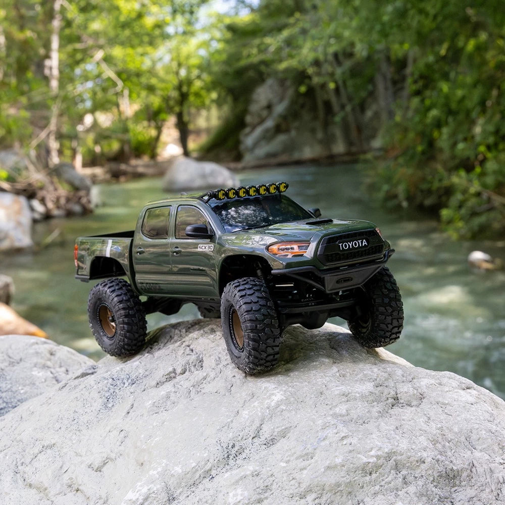 Green SCX30 Tacoma crawler with KC roof-light trim on rocks