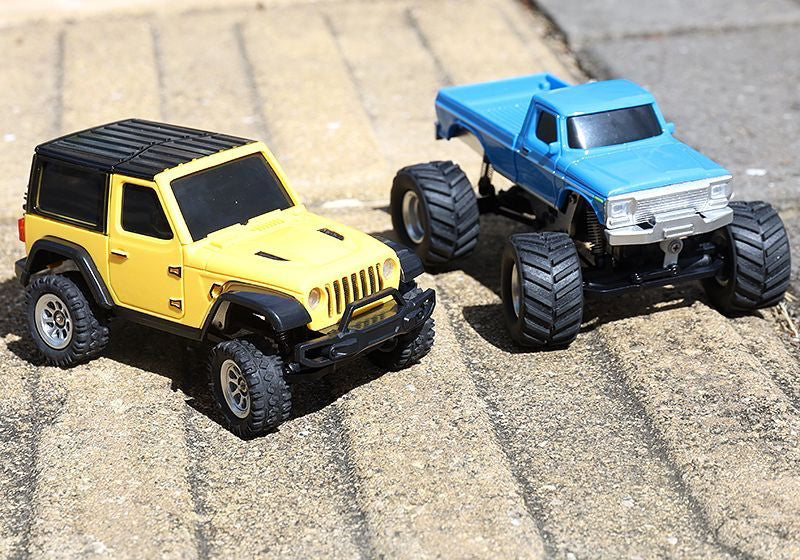 Yellow RC SUV beside a separate blue pickup in an outdoor comparison